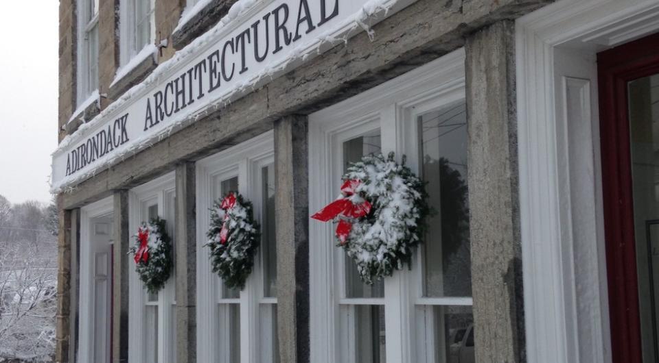 A tall stone building with white trim and winter wreaths with red bows that houses the Adirondack Architectural Heritage.