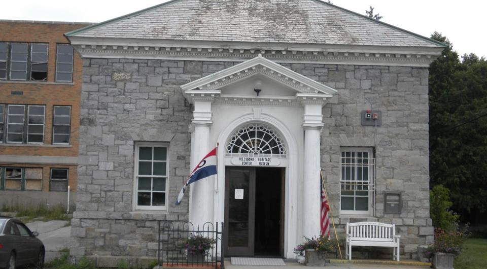 A stone building with white columns supporting the covered entry roof.