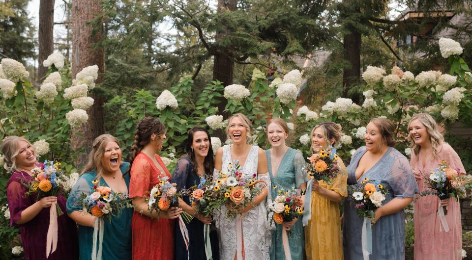 The bridal party hold colorful bouquets while wearing colorful dresses.