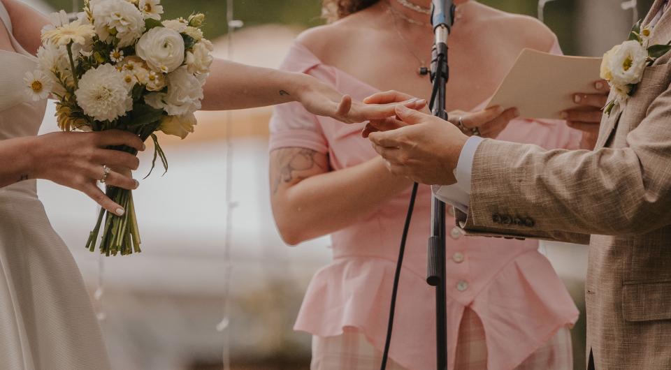 Bride holds a bouquet while she holds hands with the groom.