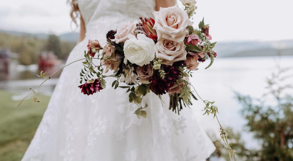 A woman in white walks by with a pink and white rose bouquet.