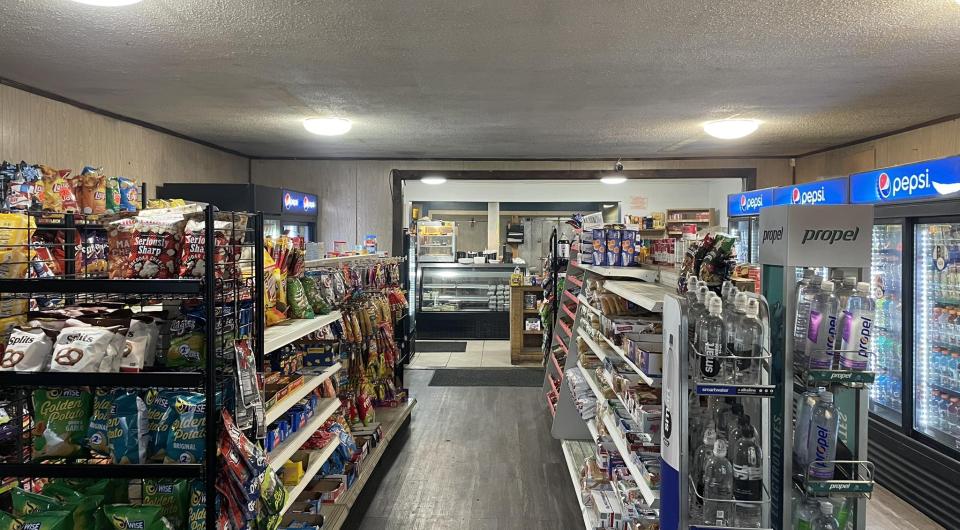 Shelves of snacks and cold drinks in coolers leading to the deli counter at Grover Hills Deli