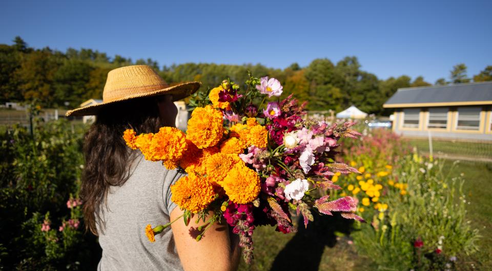 A woman in a straw hat holds a bouquet of orange and pink flowers over her shoulder.