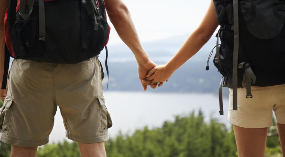 Two people hold hands while looking out over pine trees and a lake