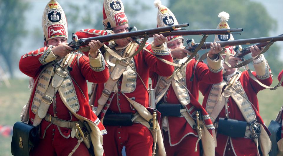 Men in period military costume fire muskets during a reenactment.