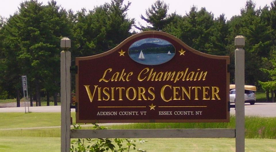 Sign for the Lake Champlain Visitors Center with gold lettering and dark stained background.