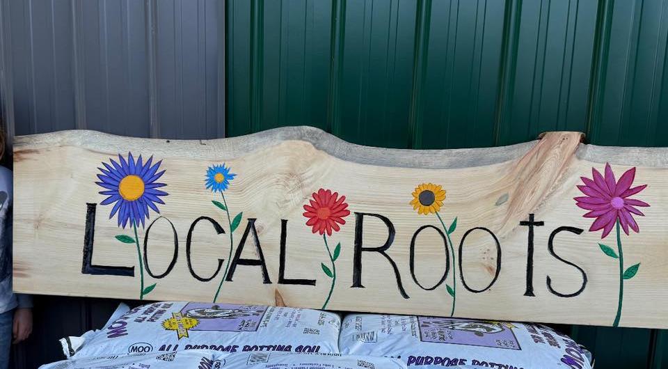 A live edge slab with Local Roots painted on it with colorful flowers