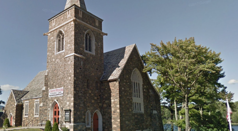 A tall stone church with high steeple on the banks of Mirror Lake.