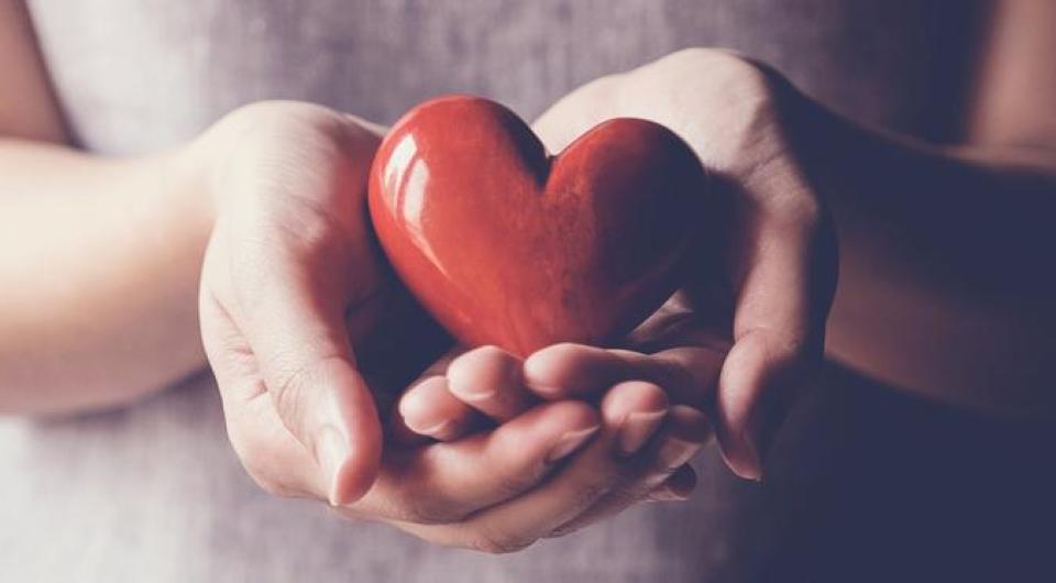 Hands holding a red heart shaped polished stone.