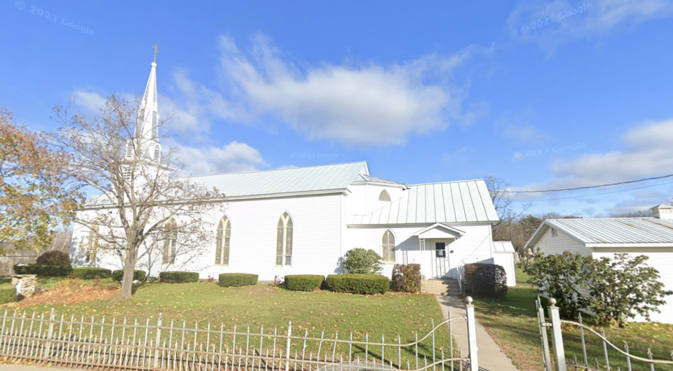 Exterior of the all white Immaculate Conception Church with tall arched windows and white wrought iron fence.