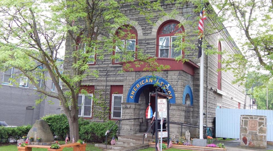 A grey stone building with red trim and a blue arched entry to the American Legion.