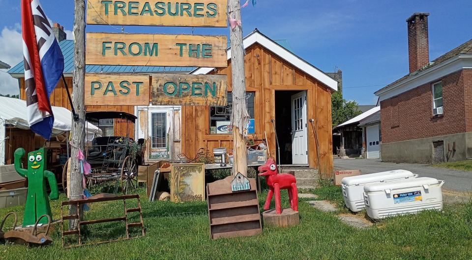 A large raw log sign posts with Treasures From The Past with an open flag flying.