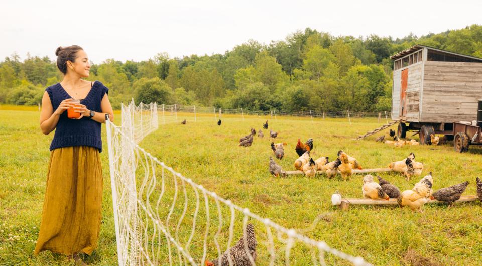 woman looks at a chicken coop with chickens around. 