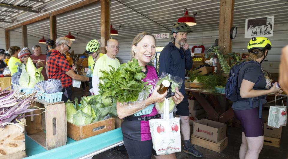 A group of people walk through a farmers market with produce in their hands. 