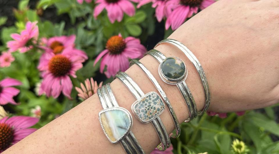A wrist with multiple hand made bracelets over a blooming pink echinacea.