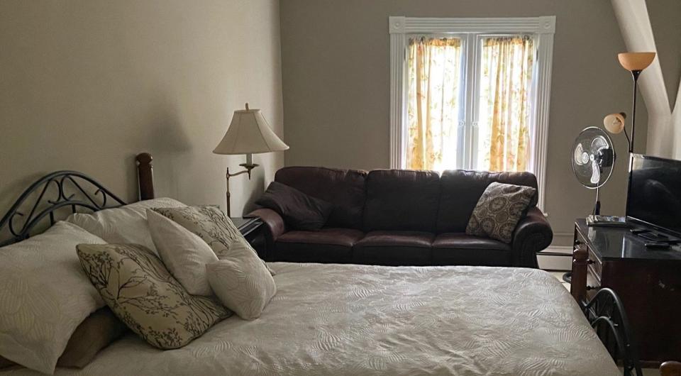A large bed with bright window and brown couch.