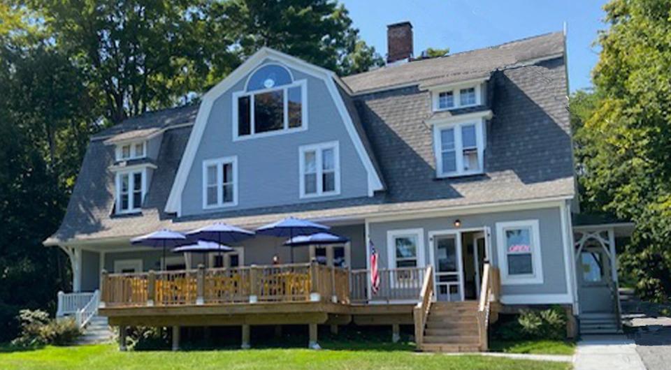 A blue building with white trim and a large deck and front lawn.