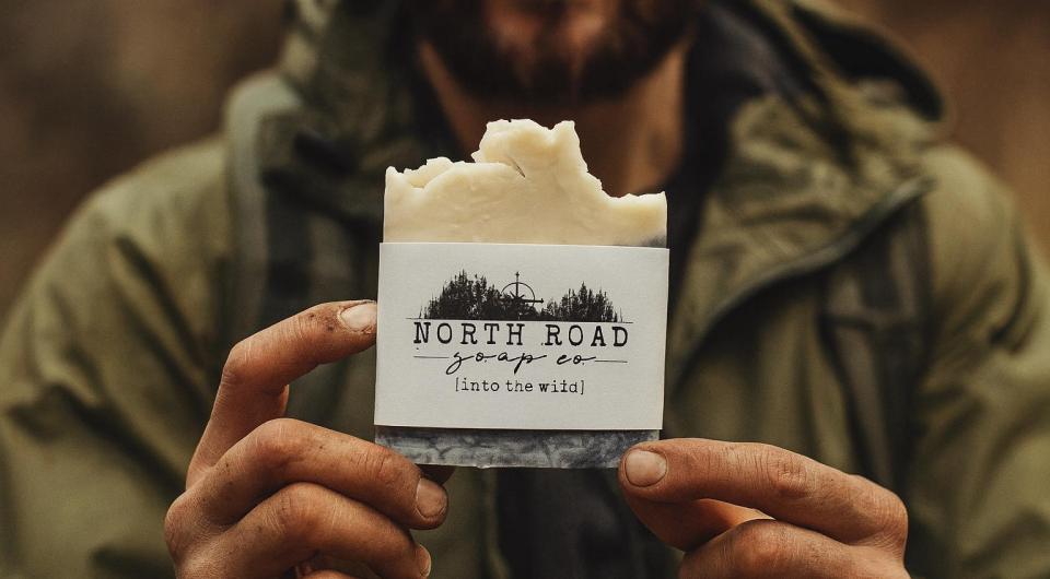 A man in a green coat holds a bar of soap out infront of him