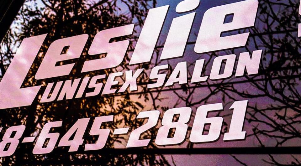 Window lettering at Leslies Unisex Salon reflecting a sunset.