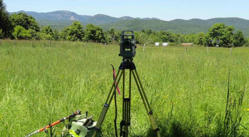 Survey equipment viewing a grassland with mountains in the background.