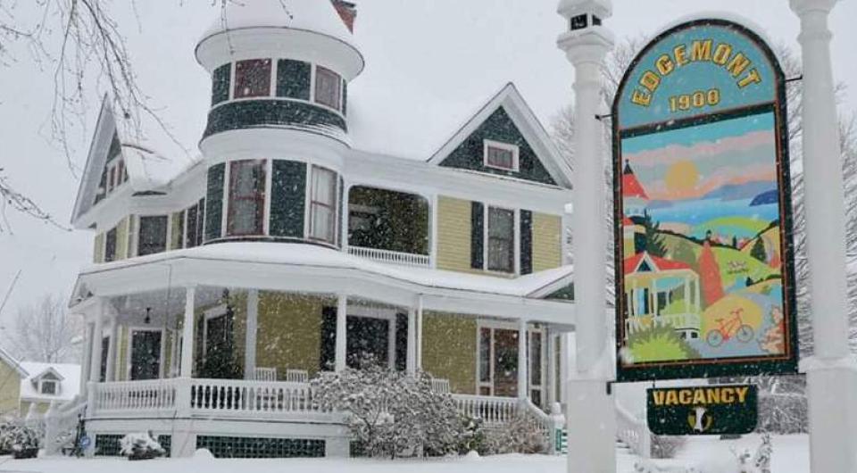 A historic home with covered porch blanketed in snow.