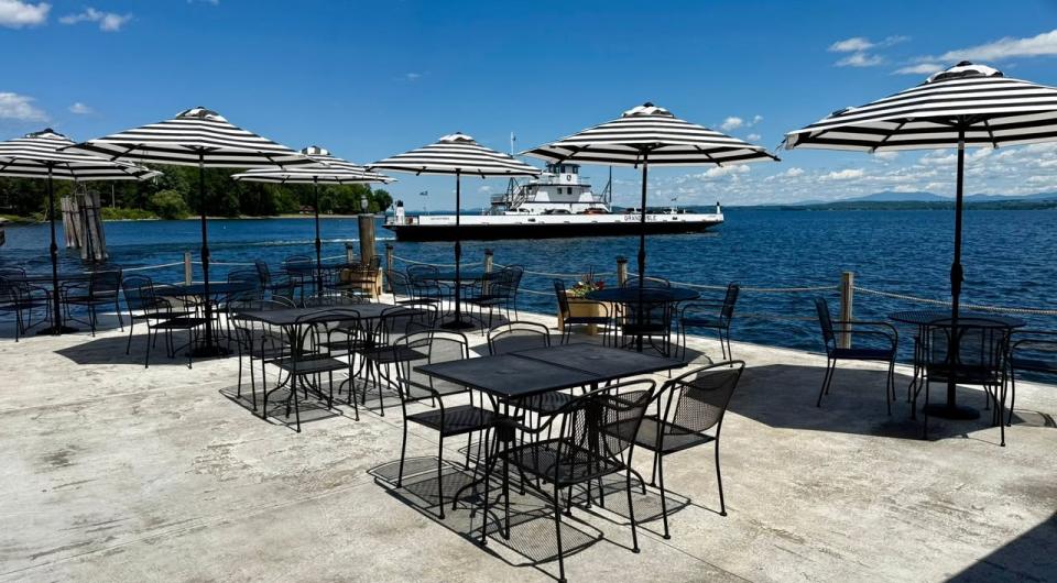 Metal tables and chairs with black and white striped sun umbrellas on the deck looking over Lake Champlain.