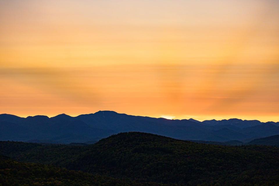 A mountain ridge is silhouetted by a bold orange sunset.