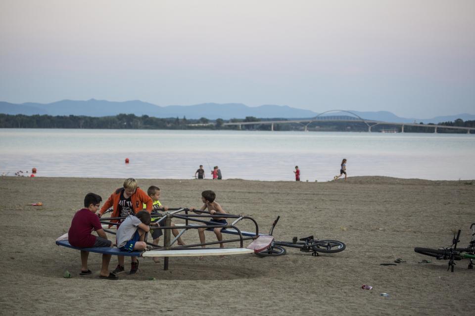 Children play on a sandy beach at dusk with a broad lake in the backgournd.