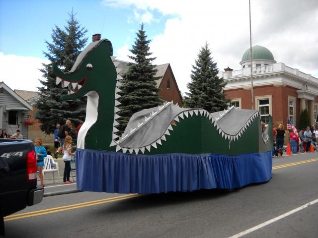 A parade float depicts a green, toothy lake monster.