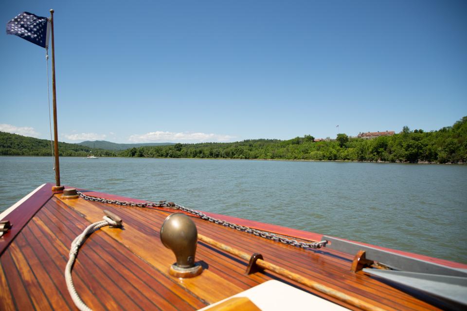 A vintage wooden motorboat on a lake on a sunny day with a stone fort on the hill beyond.