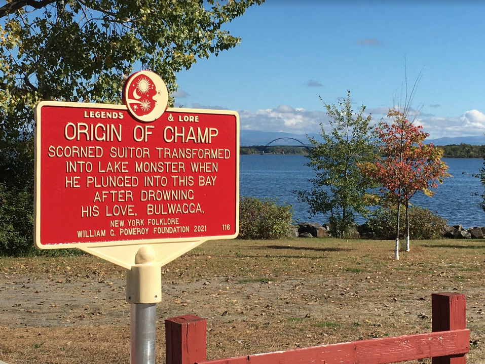 A historic marker sign overlooking a lake. The sign shares a legend of the origin of Champ.