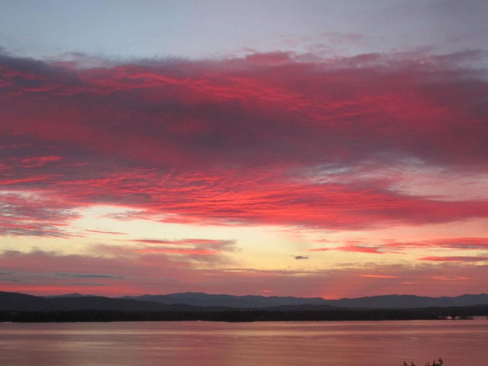 A sunset over a wide lake, with sky and water lit up in shades of pink and red.