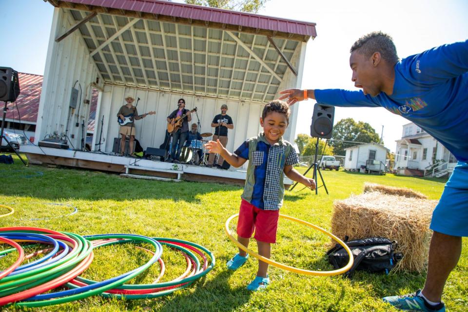 A man and boy play with hula hoops in front of an outdoor stage where a small band performs.
