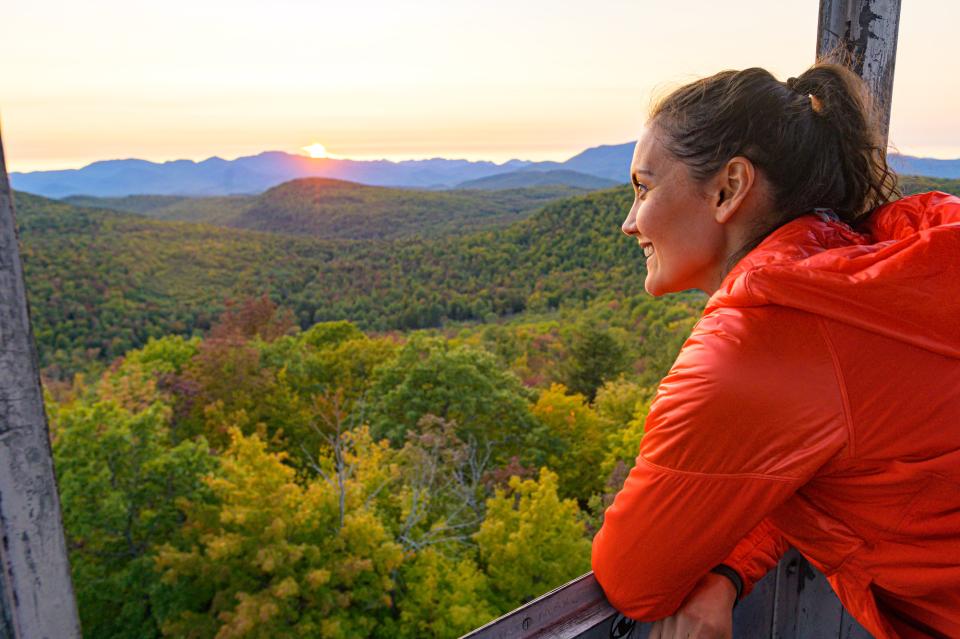 A women in a firetower overlooks the mountains during sunset