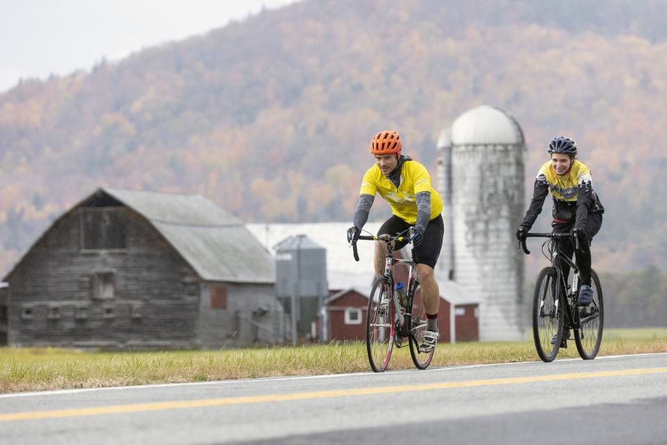 Two cyclists go past a farm during fall