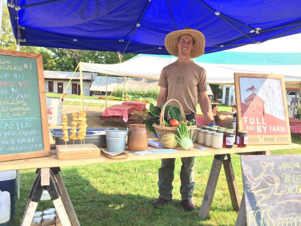 a man in a straw hat stands at a farmstand.
