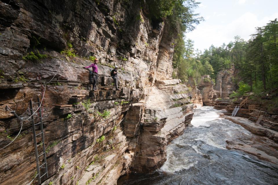 two people scale the side of a cliffside over a river.
