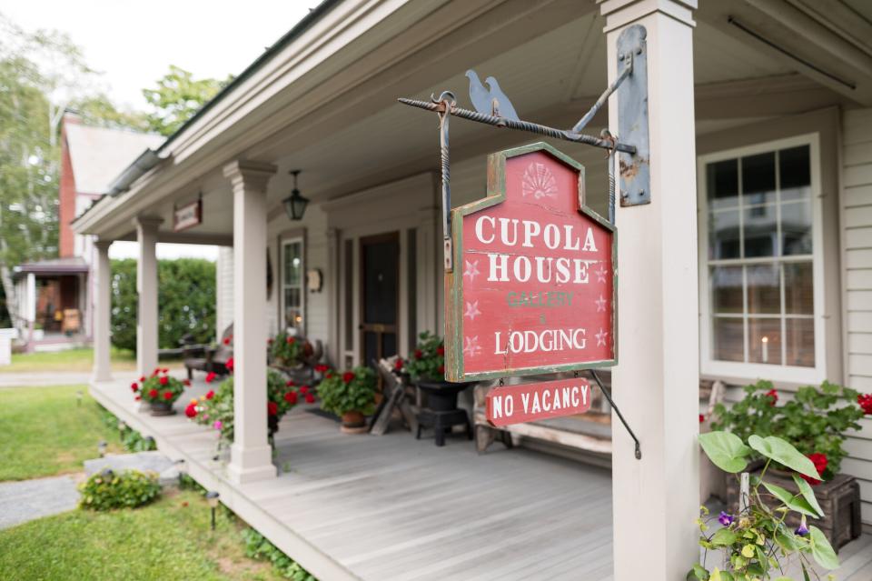 An upclose shot of a wrap-around porch with a sign that reads "Cupola House Gallery & Lodging"