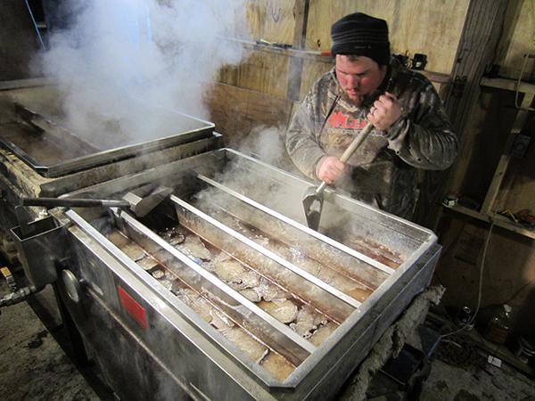 Syrup producer Kevin Sayre breaks up ice in the pans of sap above the firebox.