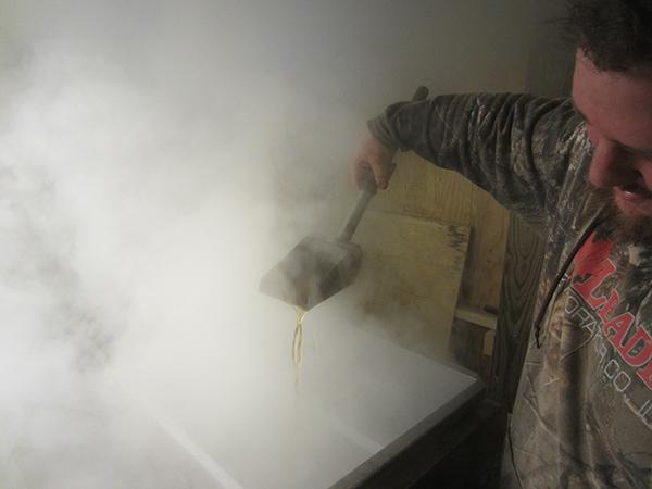 Kevin Sayre checks the syrup with a pourer amid the steam.