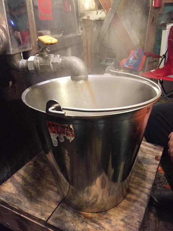 Hot maple syrup is drawn off into a large stainless stail pail.