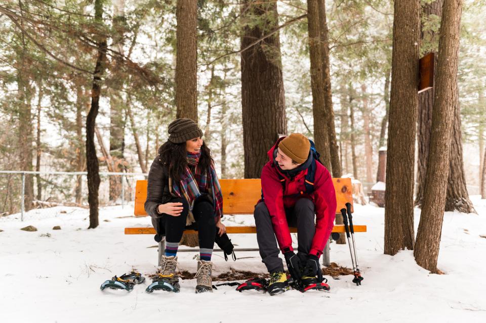 A couple sits on a bench as they secure snowshoes to their feet