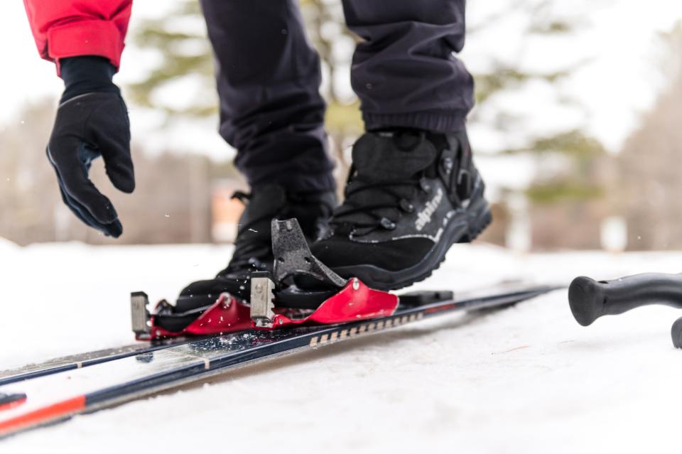 A close-up view of a person adjusting a cross-country ski binding on a snowy trail