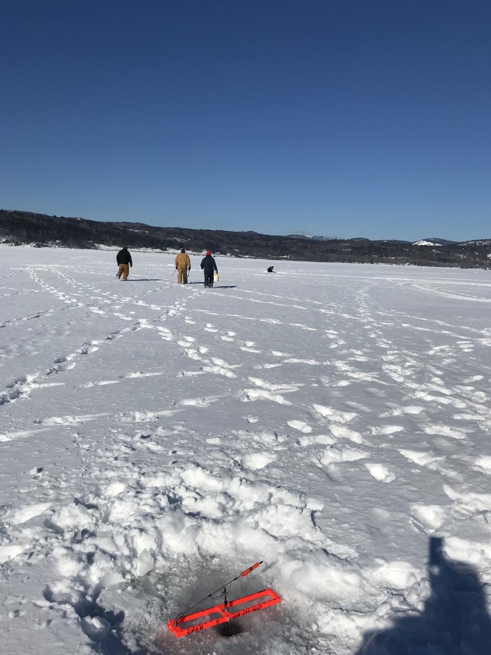 image of an expanse of frozen lake with mountains in the background and people in winter wear getting ready to ice fish