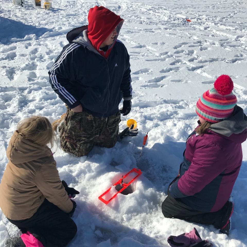 image of a group ice fishing, in a circle around a drilled hole with a pop-up
