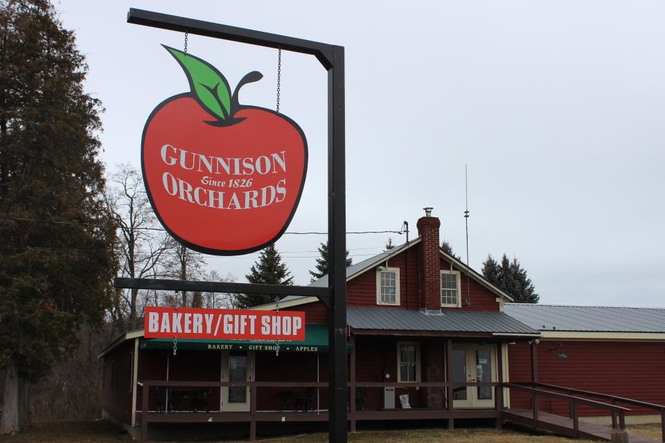 An apple-shaped entrance sign to an orchard in front of a quaint shop.