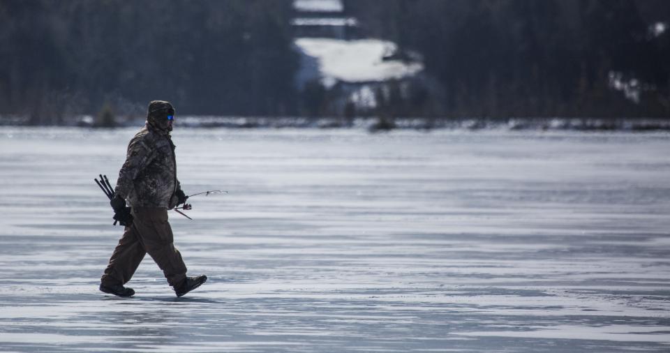 A fisherman walks across the frozen lake.
