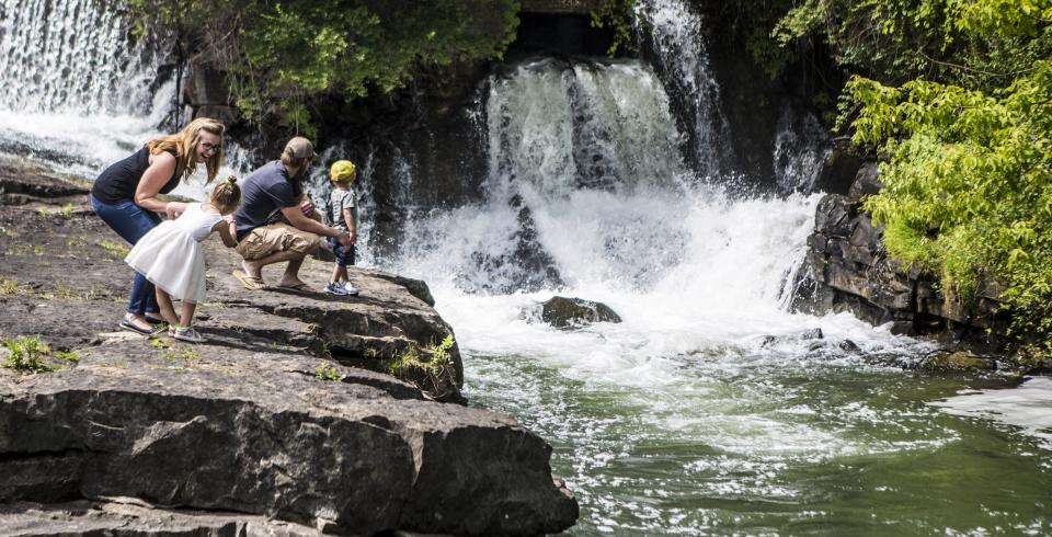 Adults and children view a rushing waterfall in the Lake Champlain Region from up close.