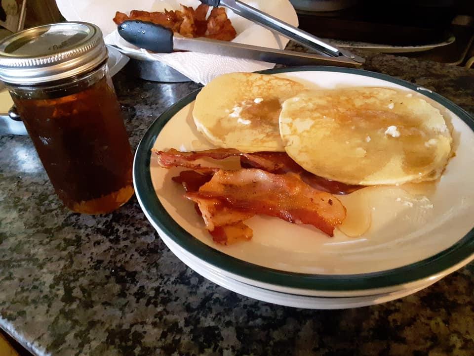 A plate of pancakes and bacon next to a jar of maple syrup.