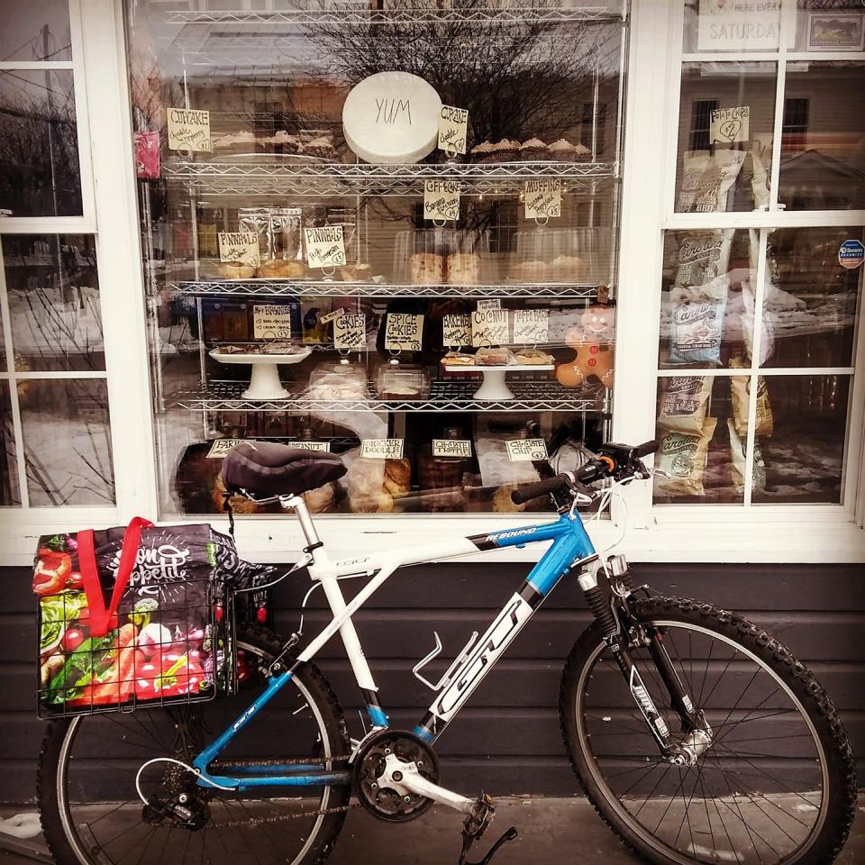 A bicycle outside a large bakery window with food on display